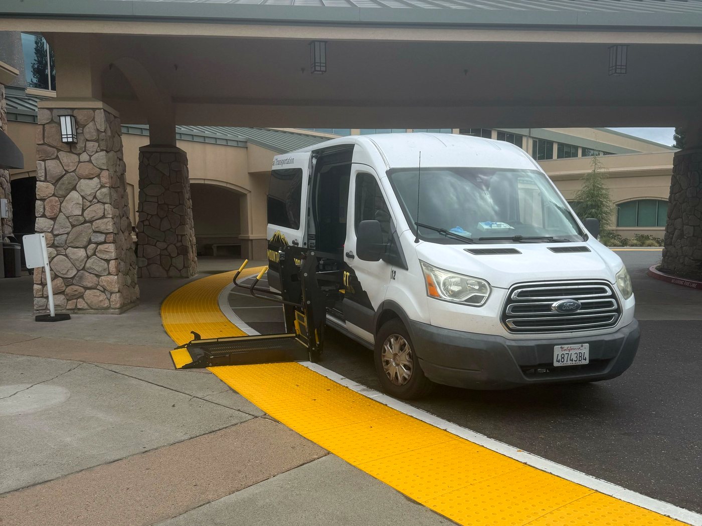 Gold Mountain Transport van with the hydraulic lift deployed at a medical facility entrance